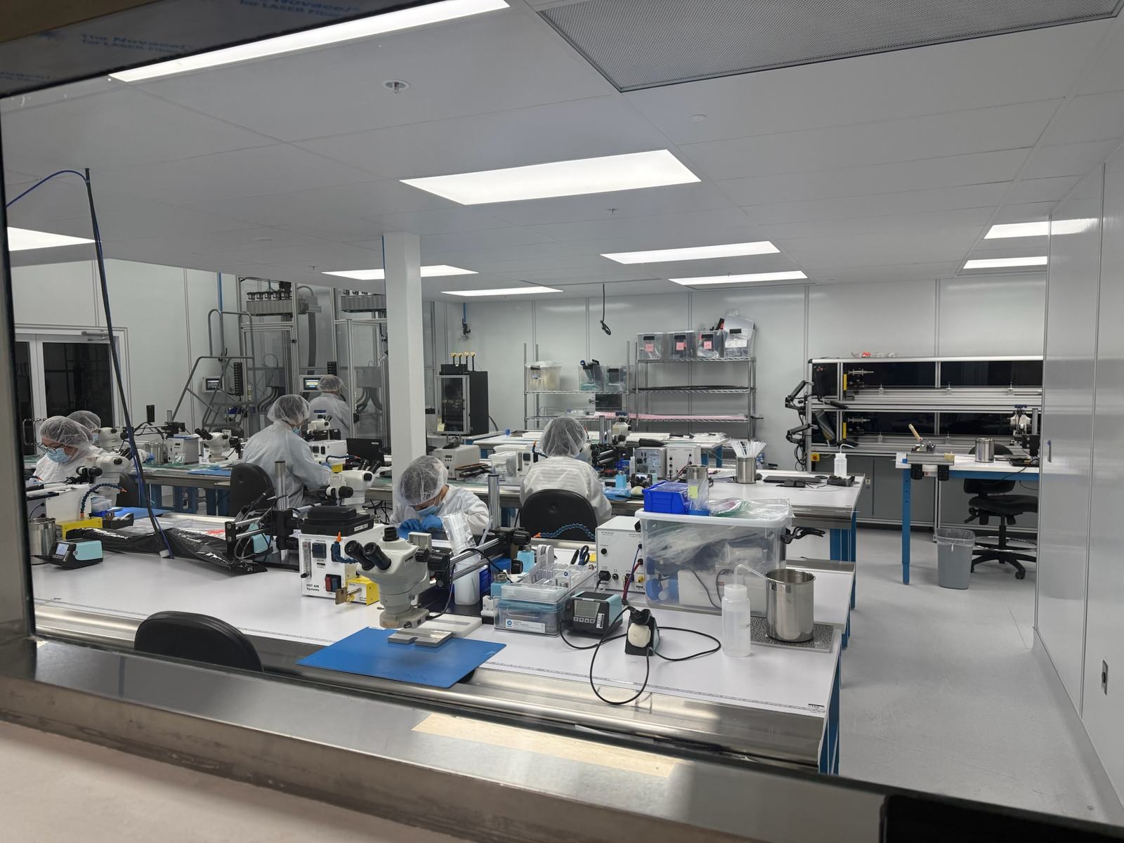 Gowned technicians assembling catheters at microscope stations on the Class 10,000 cleanroom floor