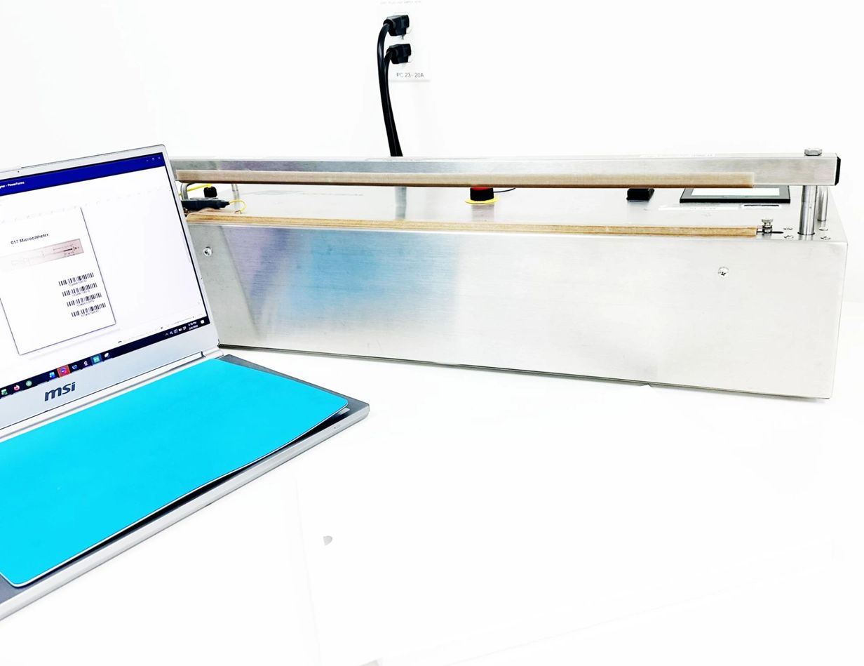 Long stainless inspection station with laptop showing microcatheter measurement data